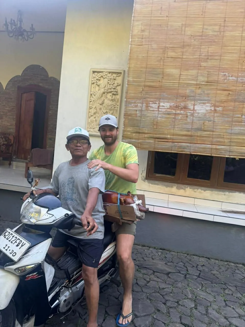 Čech nabízející služby na Bali sedí jako spolujezdec na skútru a na klíně převáží upečené sele na místní ceremonii.