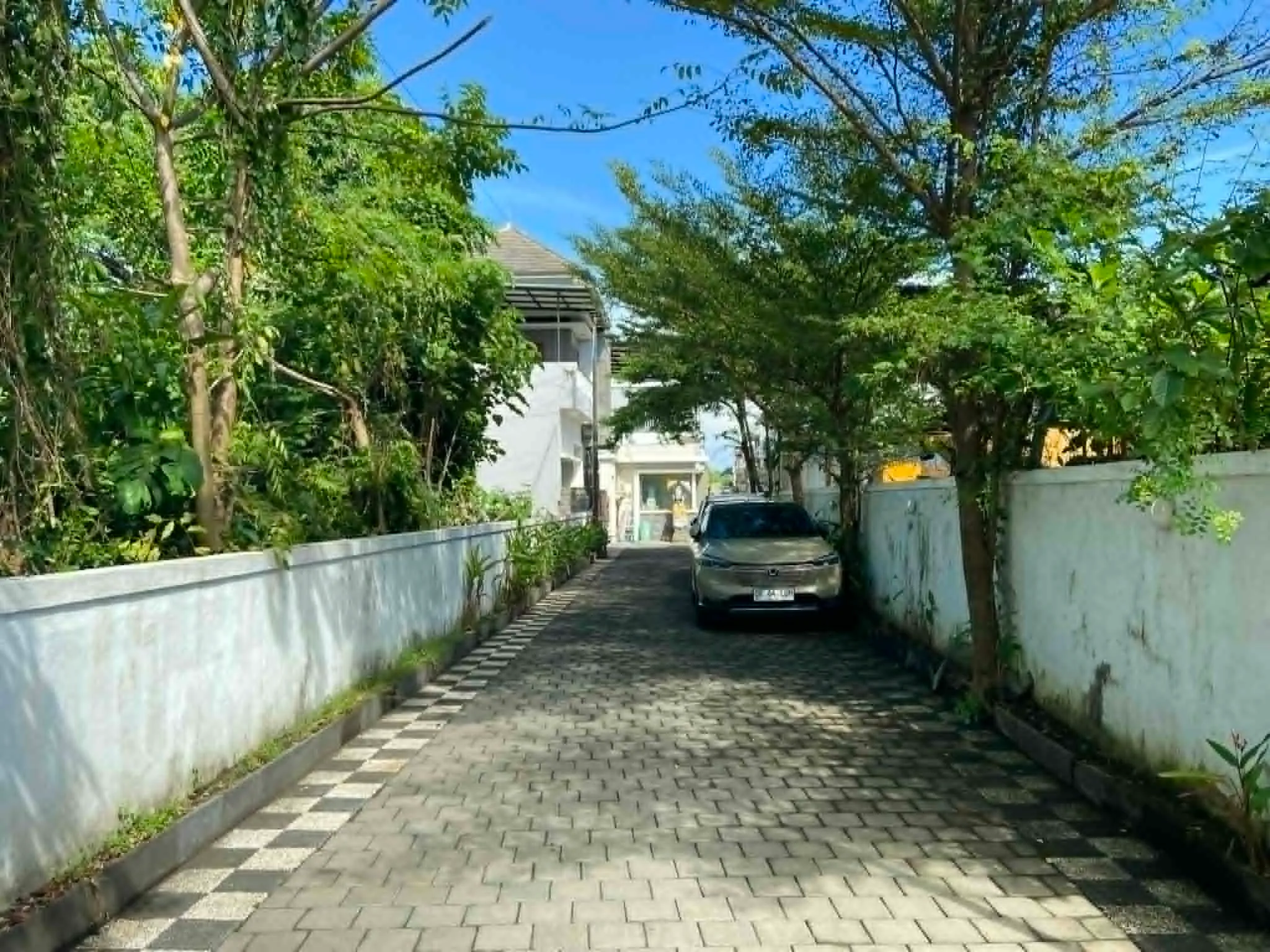Série fotografií exteriéru a interiéru čistého dvoupodlažního domu v bezpečné rezidenční čtvrti v Sanuru na Bali. Ukázka světlé ložnice, moderní koupelny a upravené ulice.