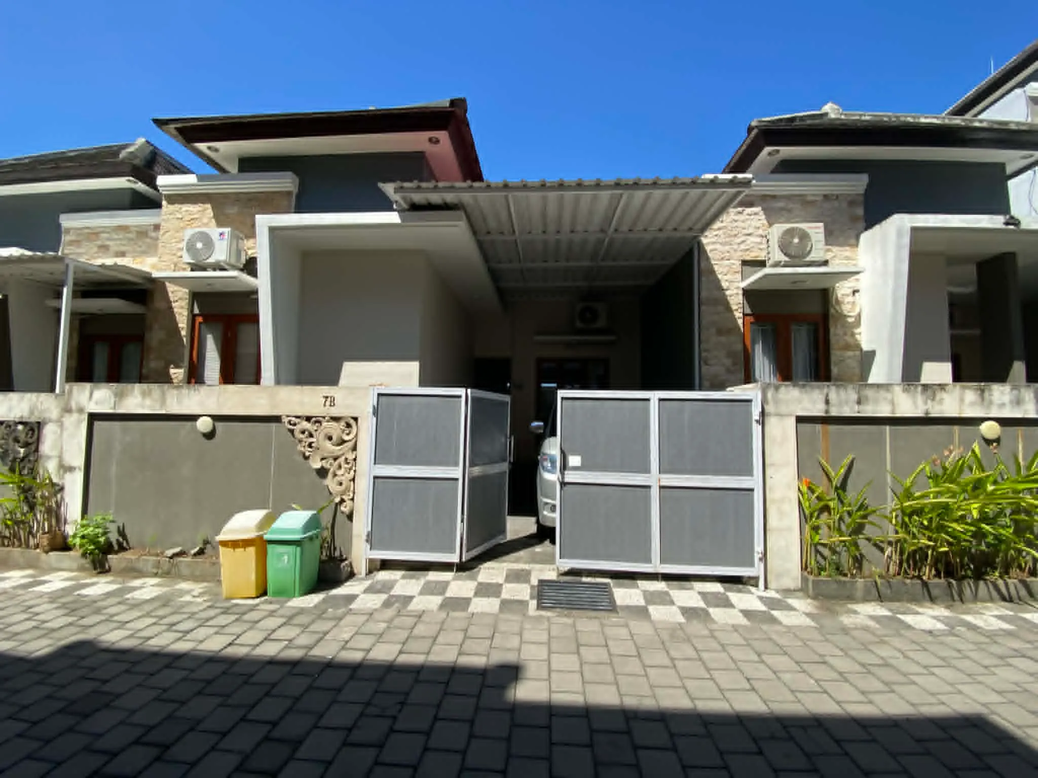 Série fotografií exteriéru a interiéru čistého dvoupodlažního domu v bezpečné rezidenční čtvrti v Sanuru na Bali. Ukázka světlé ložnice, moderní koupelny a upravené ulice.