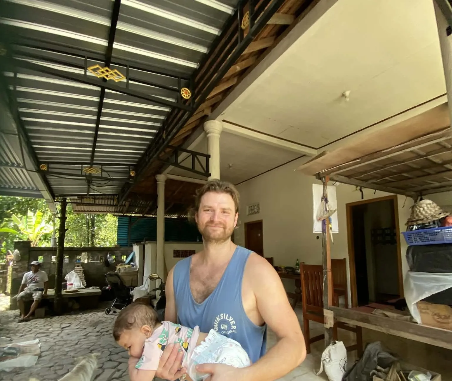 Autor projektu Bali Villa Hunter drží malé dítě na verandě lokálního domu na severu Bali.