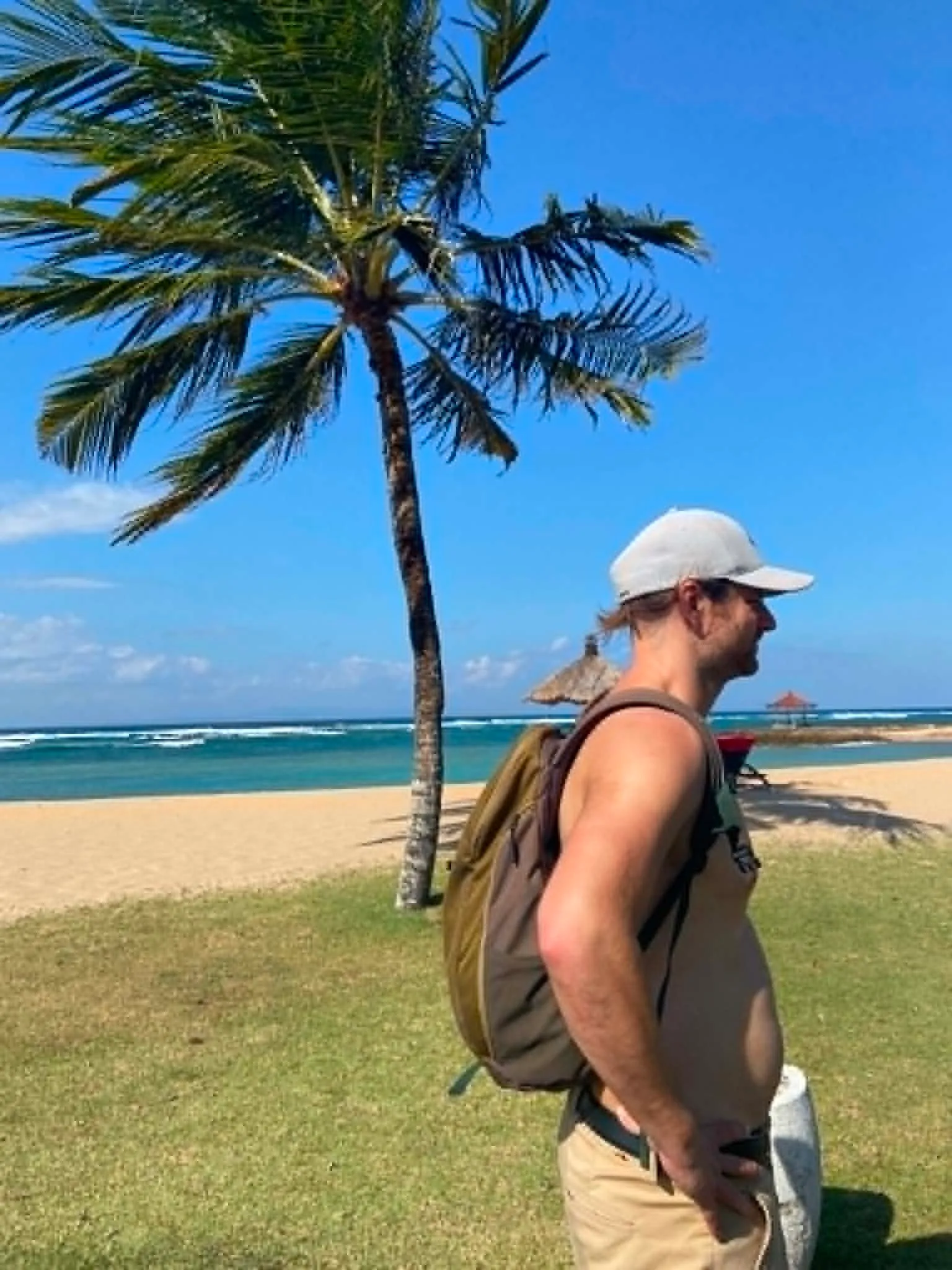 Turista s batohem na pláži Nusa Dua na Bali sleduje čisté tyrkysové moře