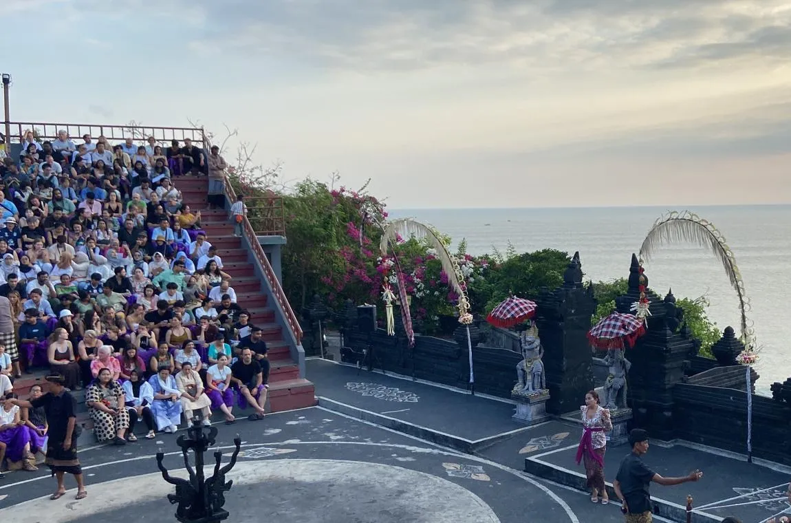Amfiteátr na útesu v Uluwatu zaplněný diváky před začátkem vystoupení Kecak, v pozadí chrámové brány a oceán