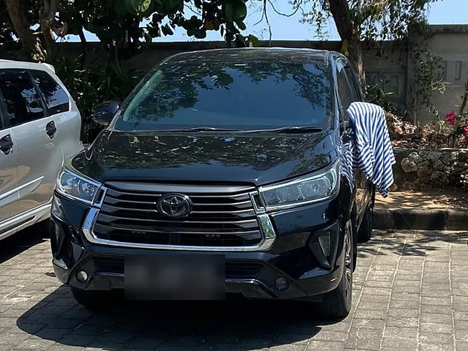 Černá Toyota Innova Reborn zaparkovaná ve stínu stromu na parkovišti u pláže na Bali