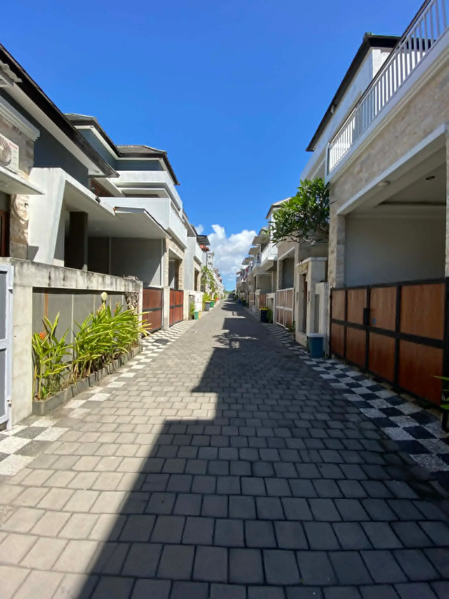 Série fotografií exteriéru a interiéru čistého dvoupodlažního domu v bezpečné rezidenční čtvrti v Sanuru na Bali. Ukázka světlé ložnice, moderní koupelny a upravené ulice.